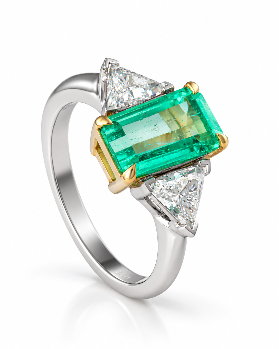 Close-up editorial photograph of an emerald-cut emerald ring with triangular diamond side stones